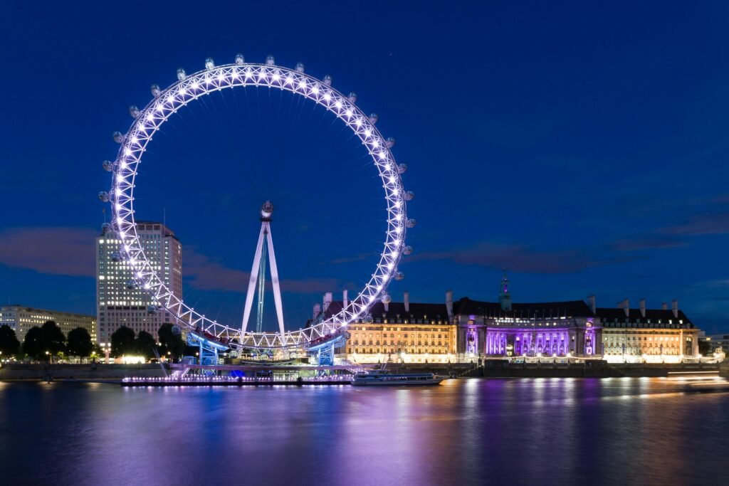 The illuminated London Eye reflects over the River Thames at night, showcasing vibrant city lights.